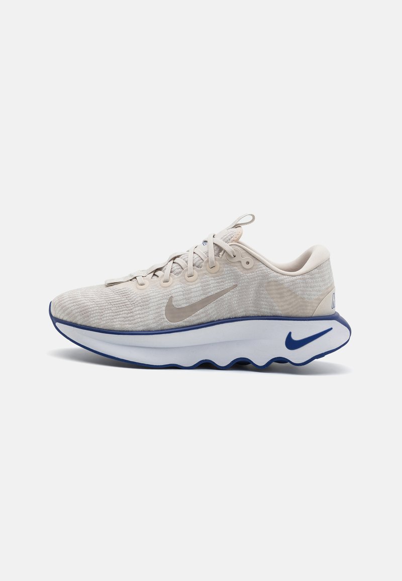 Beige sportsko med en tekstureret mesh-overdel, snørebåndslukning, polstret hvid mellemsål og blå accenter langs sålen og logoet.