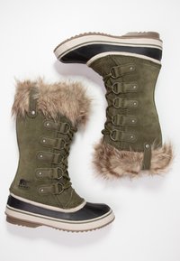 Grüne Wildleder-Winterstiefel mit einem Kragen aus Kunstfell, Schnürung vorne und schwarzen Gummisohlen. Mit grauen Akzenten und einem strukturierten Profilmuster.