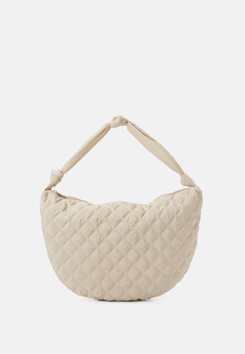 Borsa beige trapuntata con una forma arrotondata e una maniglia in tessuto annodata. Il materiale è morbido con un motivo a rombi e una chiusura a zip.