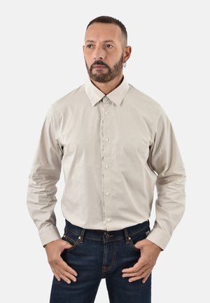 Camicia a maniche lunghe beige chiaro con design a bottoni e colletto appuntito, abbinata a jeans di denim blu scuro. Tessuto morbido, branding minimale.