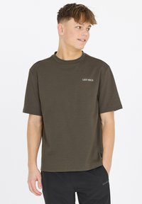 Lyhythihainen oliivivihreä t-paita, joka on valmistettu puuvillasta. Paidassa on pyöreä kaula-aukko ja pieni valkoinen logo vasemmalla rintapuolella.