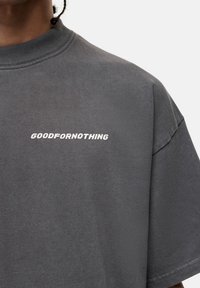 Czarnoszary bawełniany t-shirt z krótkim rękawem i okrągłym dekoltem. Posiada napis "GOODFORNOTHING" w kolorze białym, umieszczony na klatce piersiowej.