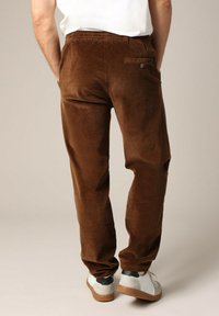Pantalons en velours côtelé marron avec une taille élastique, une poche arrière et une texture douce. Associés à des baskets blanches et noires.