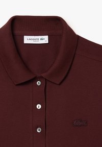 Polo shirt slim-fit Lacoste bordeaux in tessuto testurizzato. Presenta un colletto a risvolto e tre bottoni argentati, logo sul petto.