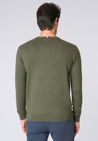 Maglione verde oliva a maglia con collo rotondo, polsini e orlo a costine. Presenta un piccolo etichetta tricolore sul colletto. Texture liscia.