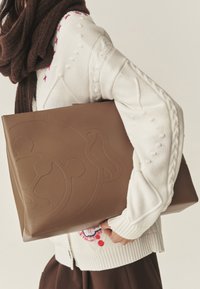 Bruine leren totebag met geprofileerd ontwerp, rechthoekige vorm en gladde textuur. Draagt bij een witte trui met kabelgebreide details.