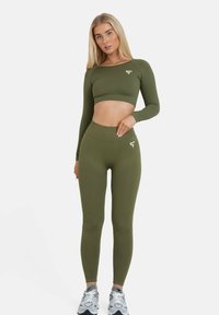 Olivengrünes langärmliges Croptop, kombiniert mit hoch taillierten Leggings. Verfügt über eine gerippte Textur und ein Logo-Detail in Weiß. Sportlicher Schnitt.