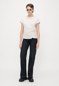 Light beige short-sleeve t-shirt with a front twist detail, paired with high-waisted black jeans, and chunky black shoes.