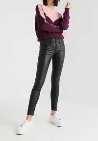 Černé úzké kalhoty z umělé kůže kombinované s barevně blokovaným svetr s fialovými a růžovými odstíny. Outfit doplňují bílé tenisky.