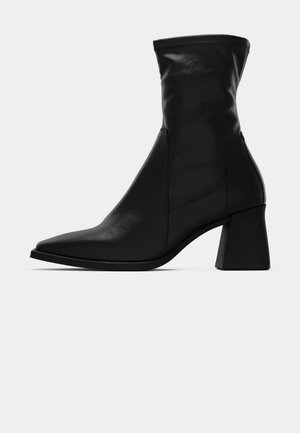 Bottines noires à bout pointu, en cuir lisse. Elles présentent un talon carré et une tige ajustée, avec des détails de couture visibles.
