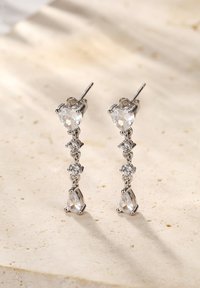 Pendientes colgantes que presentan gemas transparentes en forma de corazón y gota, montadas en metal de tono plateado con pequeñas piedras redondas de acento.