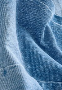 Tessuto denim di un blu chiaro, che mostra una texture liscia con sottili variazioni di tonalità e un leggero aspetto drappeggiato.