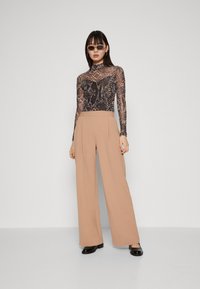 Svart langermet bodysuit med slangeskriftmønster, sammen med beige vide bukser. Svart glansete sko. Solbriller fullfører antrekket.
