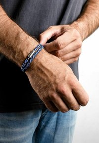 Modra in bela pletenica z metalnim zapiralom, nosi se na zapestju. Zapestnica ima teksturiran vzorec in več niti.