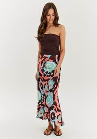 Hnedý top bez ramienok v kombinácii s dlhou farebnou sukňou s výrazným kvetinovým vzorom v ružovej, tyrkysovej a hnedej farbe. Model nosí ploché sandále.