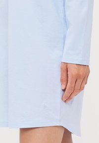 Ljusblå långärmad klänning i bomullsmaterial med en liten broderad design vid fållen. Slät textur med en avslappnad passform.