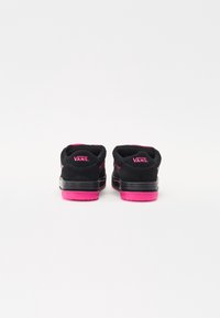 Mustat mokkanahkakengät Vans-merkiltä vaaleanpunaisilla yksityiskohdilla. Paksu pohja on vaaleanpunaista kumia. Minimalistinen muotoilu, pyöreä takakappale ja logo näkyvissä.