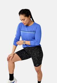 Sinine pikakä sleevesportline särgiga, millel on horisontaalne triipude disain, koos mustade loomade mustriga lühikeste pükste vahel. Kanga tundub kerge ja sobiv.