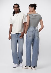 Avslappede lyseblå denimjeans med høy midje og falming. Modellen har på seg en grå kort topp. Har en hvit merkeetikett bak.