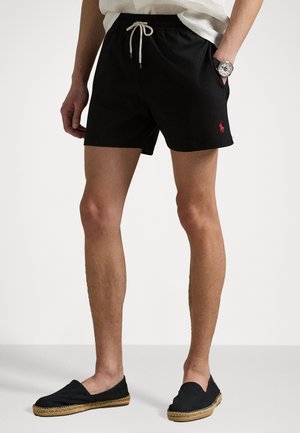 Black swim shorts with an elastic waistband and drawstring, featuring a small red logo on the left side. Smooth fabric and relaxed fit.