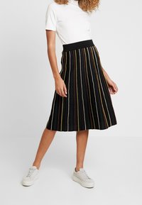 Gonna nera plissettata con strisce verticali multicolori, una ampia vita elasticizzata, abbinata a una maglietta attillata bianca e sneaker bianche.