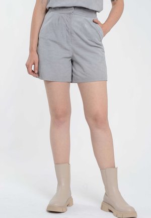 Lys grå shorts i et blødt stof med en glat tekstur, med sidelommer og et taljebånd. Parret med beige ankelstøvler.