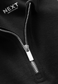 Schwarze Zip-Hoodie mit silbernem Reißverschluss und strukturiertem Stoff. Sichtbares "NEXT"-Label, das das Markendetail hervorhebt.
