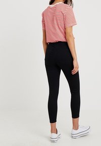 Černé těsně přiléhající džíny v kombinaci s červeno-bílým pruhovaným tričkem, které má krátké rukávy a kulatý výstřih. Celkový vzhled doplňují bílé tenisky.