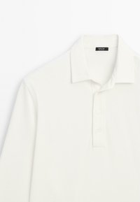 Hvid langærmet polo skjorte lavet af blødt stof, med krave, fire knaplukninger og en glat tekstur.
