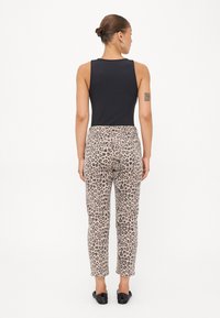 Bodysuit negro sin mangas combinado con pantalones beiges de estampado de leopardo, con un diseño ajustado y pierna ligeramente entallada. Se llevan zapatos negros.