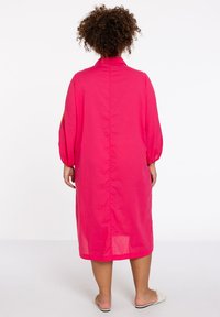 Rosa, knielanges Kleid mit lockerer Passform, langen Puffärmel und einem Kragen. Hat eine einfarbige Textur und eine zentrale Naht im Rücken.