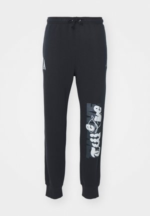 Pantalon de survêtement noir avec taille élastique et cordon de serrage, présentant des motifs graphiques blancs le long de la jambe gauche et des poignets côtelés.