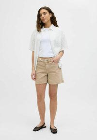 Camicetta bianca a maniche corte con ricami, indossata sopra una maglietta bianca semplice, abbinata a pantaloni corti beige e scarpe flats nere in rete. Design semplice e vestibilità casual.