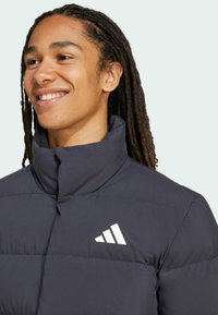 Navy puffer jacket with high collar, featuring a white logo on the chest and quilted texture. Smooth material, designed for warmth.