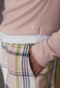 Light pink long-sleeve top with a small branded tag, paired with plaid pants featuring green, blue, and pink stripes, and side pockets.
