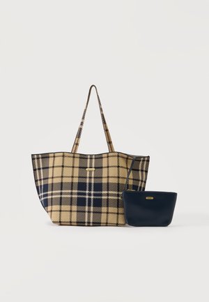 Geantă mare beige și bleumarin cu model în carouri, cu bretele lungi, lângă o borsetă solidă bleumarin mai mică, cu curea pentru încheietură, ambele cu etichete mici aurii ale brandului.