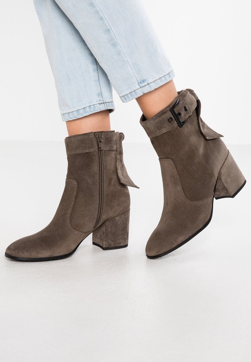 Bottines en daim marron à talons blocs, fermeture éclair latérale et détail boucle, portées avec un jean court bleu clair.