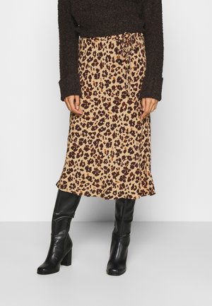 Femme portant une jupe midi imprimé léopard avec une taille nouée, des bottes à talons noires montantes jusqu'aux genoux, et un pull texturé marron foncé.