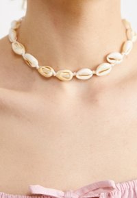 Collier ras du cou en coquillages blancs avec des accents beige naturel, présentant une texture lisse et un design simple et incurvé.