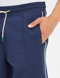 Granatowe dresy o miękkiej fakturze, z białym paskiem po bokach, elastycznym paskiem w talii i sznurkiem ściągającym w zielonym kolorze.