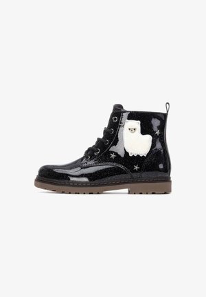 Botas de tobillo de charol negro con superficie brillante, que presentan un apliqué de oveja esponjosa blanca y pequeños detalles en forma de estrella en el lateral. Suela de goma marrón.