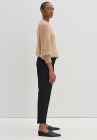 Pull léger beige, fluffy, avec des manches trois-quarts, associé à un pantalon noir ajusté et des mocassins noirs à talon pointu. Design simple et texturé.