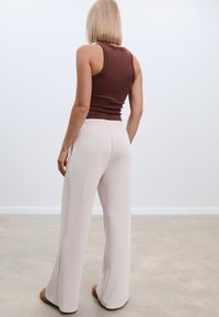 Brauner, figurbetonter Tank-Top, kombiniert mit hellbeigen, weiten Hosen; glattes Material mit lockerer Passform und elastischem Bund.