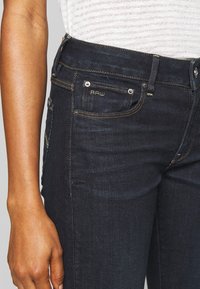 Mörkblå denimjeans med slim fit, med sömnadsdetaljer och en liten broderad "RAW"-logotyp på framfickan.