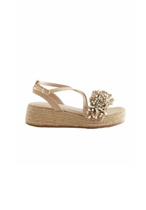 Sandale espadrille beige avec une semelle compensée en jute tressé, ornée d'un accent floral en fibres naturelles et petites perles blanches. Bride de cheville réglable.