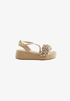 Beige espadrille sandaal met een gevlochten jute sleehak, voorzien van een bloemaccent gemaakt van natuurlijke vezels en kleine witte kralen. Verstelbare enkelband.