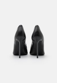 Chaussures à talons hauts en cuir noir avec un bout pointu et un design élégant. Texture lisse avec une finition brillante et des talons aiguilles.