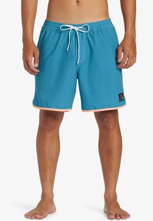 Blue swim trunks made of lightweight fabric with an elastic waistband and white drawstring. Features orange trim at the hem and logo patch.
