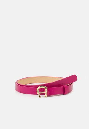 Dünner rosa Ledergürtel mit goldener Hufeisenförmiger Schnalle, flach liegend mit leicht angehobener Spitze auf weißem Hintergrund.