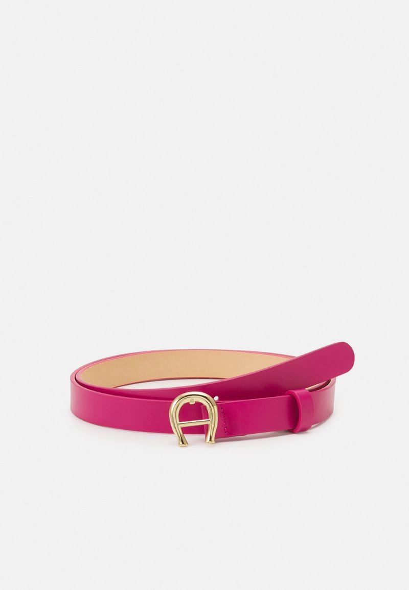 Ceinture fine en cuir rose avec une boucle dorée en forme de fer à cheval, posée à plat avec la pointe légèrement relevée sur un fond blanc.